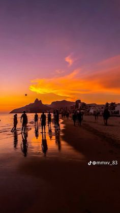 people walking on the beach at sunset with mountains in the backgrounnds