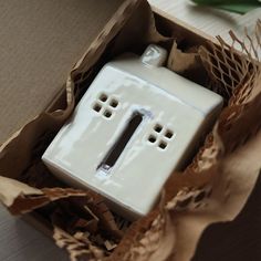 a white ceramic house in a box with brown tissue paper around it's edges