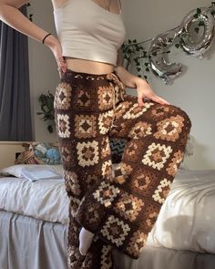 a woman standing on top of a bed wearing brown pants