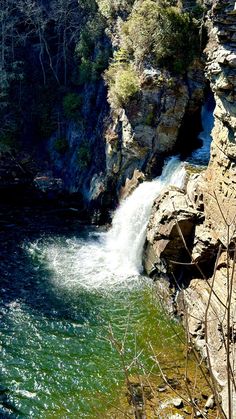 there is a small waterfall coming out of the side of a cliff next to a body of water