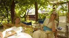 two women sitting in chairs under a tree