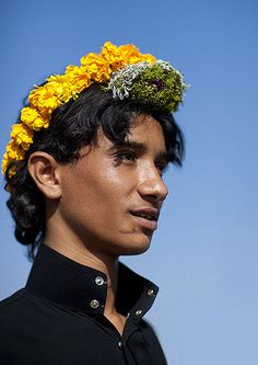 a young man with a flower crown on his head looking off to the side in front of a blue sky