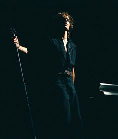 a man standing on top of a stage holding a microphone in his right hand and wearing black pants