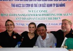 four people sitting at a table with a banner behind them that says welcome to da nang center supporting for agent and disabled children