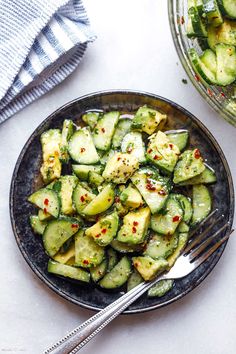 a bowl filled with cucumbers next to a fork and spoon on top of a table