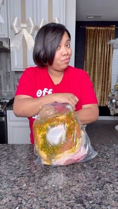 a woman in a red shirt holding a bag of food on top of a counter