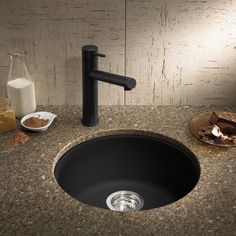 a black sink sitting under a faucet next to a bowl of cereal and milk