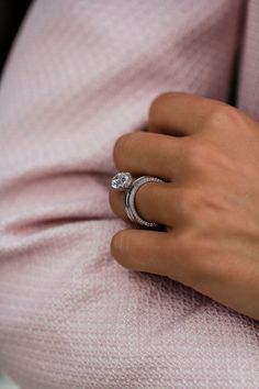 a woman's hand with a ring on her finger and a pink sweater behind her