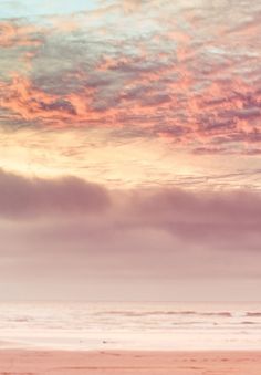 two people walking on the beach with surfboards under a pink and blue sky at sunset