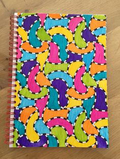 a notebook with colorful designs on it sitting on top of a wooden table next to a pen