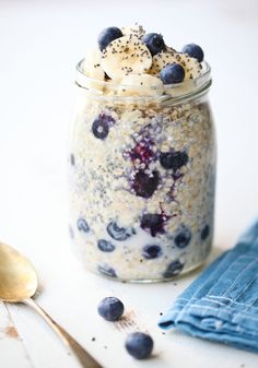 a glass jar filled with oatmeal and blueberries next to a spoon