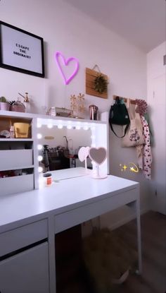 a white desk topped with lots of drawers under a neon heart shaped wall hanging on the wall