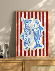 two fish are on a red and white striped wall next to a wooden cabinet with books