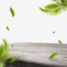 a wooden table topped with lots of green leafy plants and leaves flying in the air