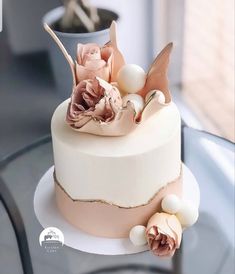 a white and pink cake with flowers on top sitting on a glass table next to a potted plant