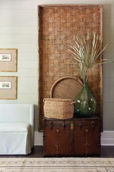 a wicker basket sitting on top of a trunk next to a vase with plants in it