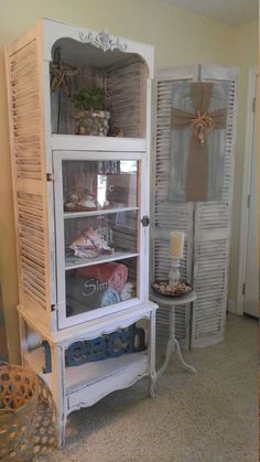 an old china cabinet is painted white and has decorative items on the top shelf, along with a candle