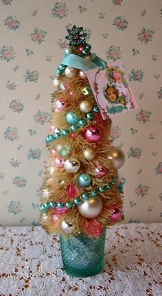 a small christmas tree in a glass vase on a table next to a wallpapered wall