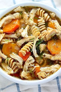 a white bowl filled with chicken noodle soup on top of a blue and white towel