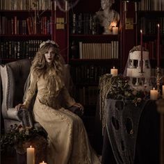 a woman sitting on a chair in front of a bookshelf filled with candles