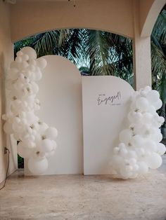 an arch made out of balloons with the word engaged written on it in front of palm trees