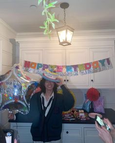 a woman in a party hat is holding up balloons and confetti to her face