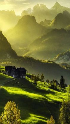 the sun shines brightly on green hills and houses in the distance, with mountains in the background