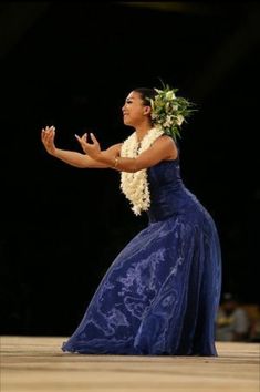 a woman in a blue dress standing on top of a wooden floor with her arms outstretched