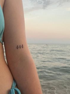 a woman's arm with the number forty four tattooed on it, in front of the ocean