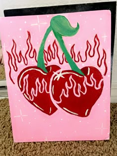 two cherries with flames on pink paper and black frame, sitting on carpet next to white wall