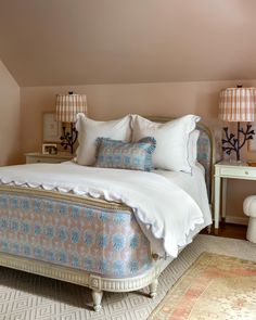 a bed with white sheets and pillows in a bedroom next to two lamps on either side of the bed