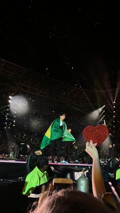 a person holding up a heart shaped object in front of an audience at a concert