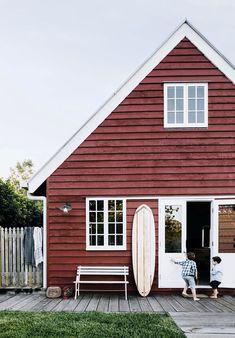 a man standing in front of a red house with a surfboard leaning against the door