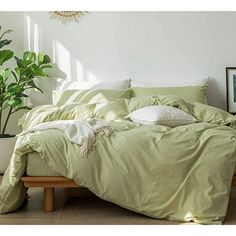 a bed with green sheets and pillows in a room next to a potted plant