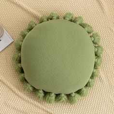 a round cushion with pom - poms sits on a bed