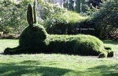 an animal made out of grass sitting on top of a lush green field next to trees