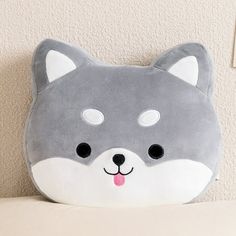 a gray and white stuffed animal pillow on top of a bed next to a wall