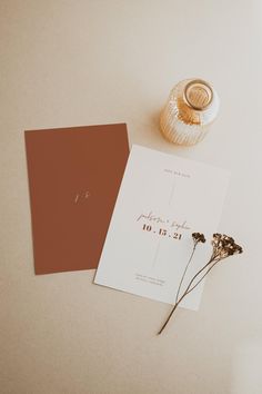 the wedding stationery is laid out next to a vase with dried flowers on it