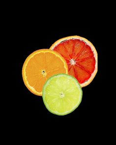 three oranges, one lime and one grapefruit cut in half on a black background