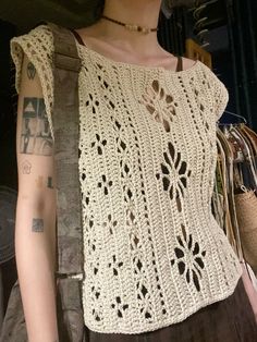 a mannequin wearing a white crochet top and brown pants with tattoos on her arm