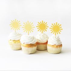 four cupcakes with white frosting and yellow sunburst toppers on them