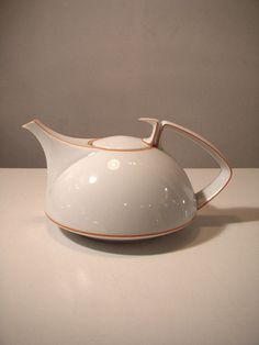 a white tea pot with an orange stripe on it