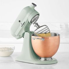 a green mixer with an orange bowl next to it on a white counter top,