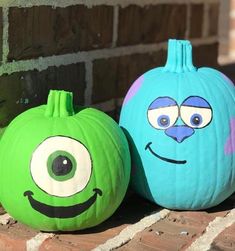 two pumpkins with faces painted on them sitting next to each other in front of a brick wall