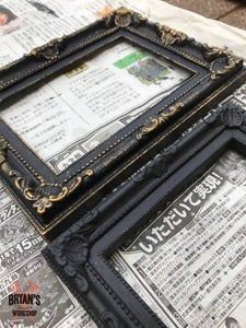 an ornate black frame sitting on top of news paper next to a pair of scissors