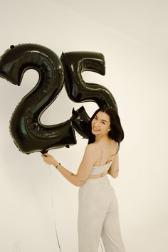 a woman holding two black balloons in front of her face and the number twenty five