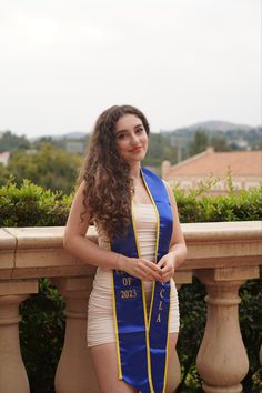 a woman in a blue and yellow graduation gown standing on a balcony with her hand on her hip