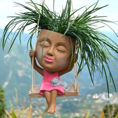 a clay figurine hanging from a tree with a plant in it's head