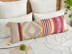 a pillow with tassels and a book on top of a bed next to pillows