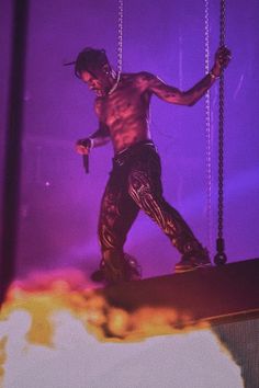 a man with no shirt on performing in front of a purple and yellow background at a concert